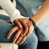 two hands wresting on a leg with silicone rings on their fingers